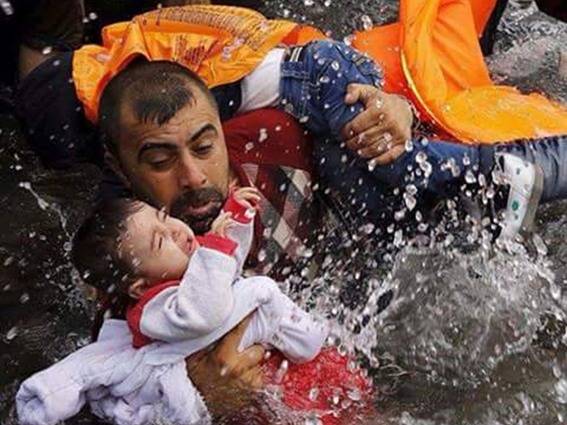 صورة مؤثرة.. لاجئ سوري يحمل طفليه في البحر للوصول إلى اليونان