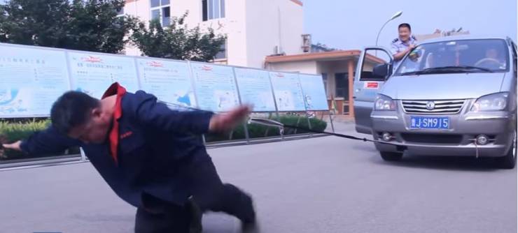 فيديو:  صيني يسير بحذاء وزنه 300 كيلو جرام ويسحب سيارة برقبته!