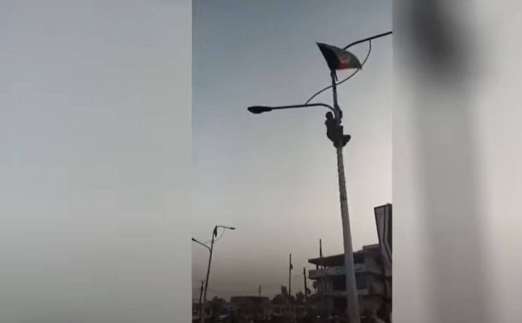 رجل يصعد على عمود إنارة لرفع العلم الأفغاني في جلال أباد